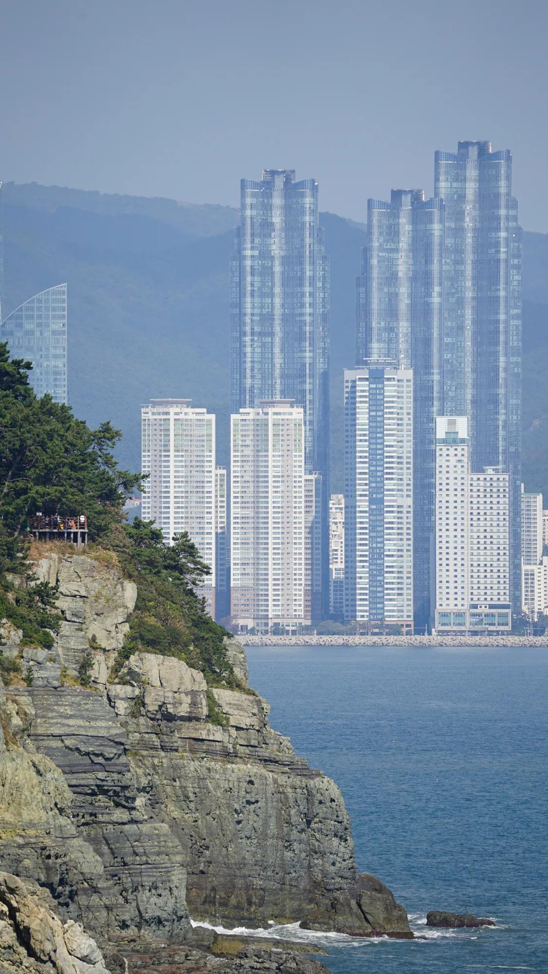 Felsküste vor Hochhäusern und bewaldeten Hügeln in Busan