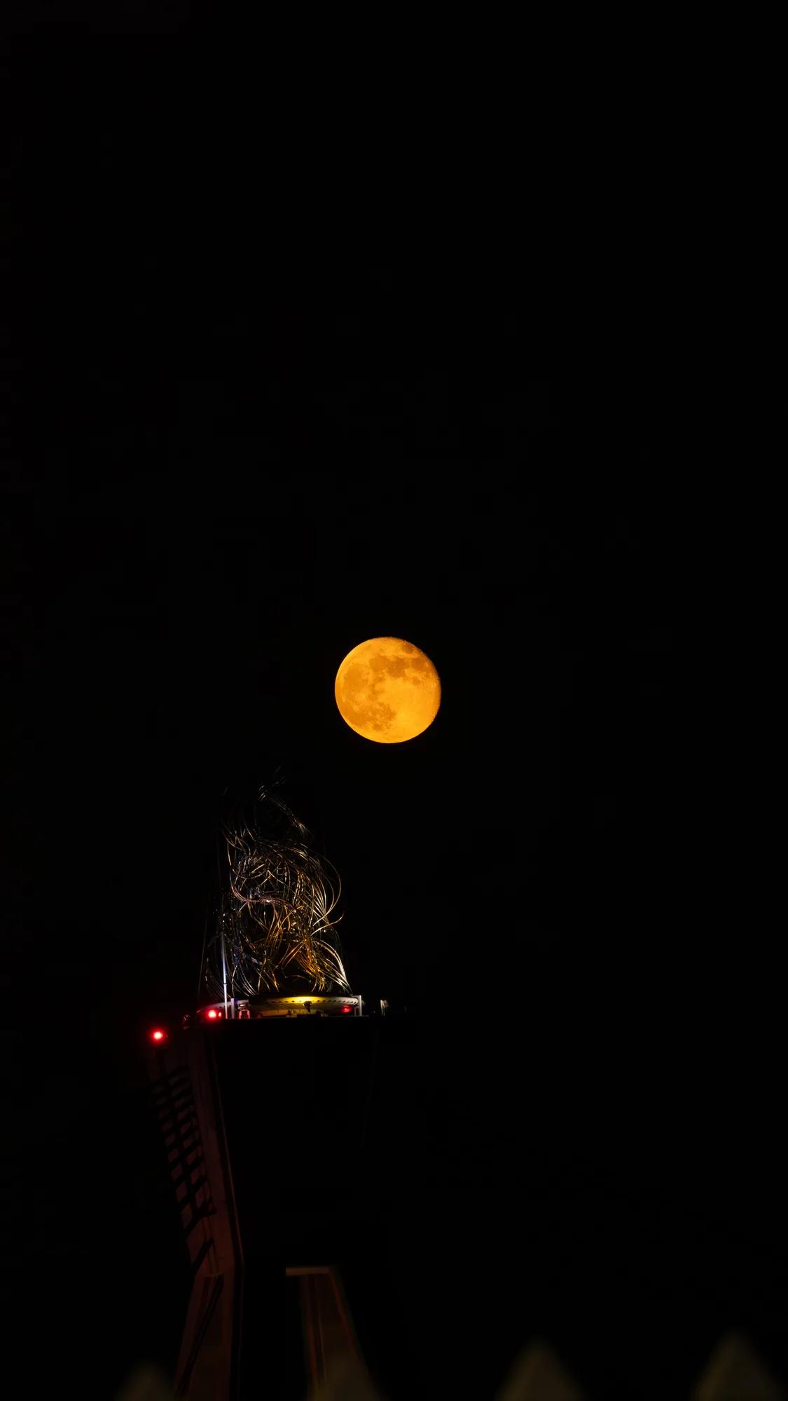 Orangefarbener Mond über der Spitze eines beleuchteten Turms
