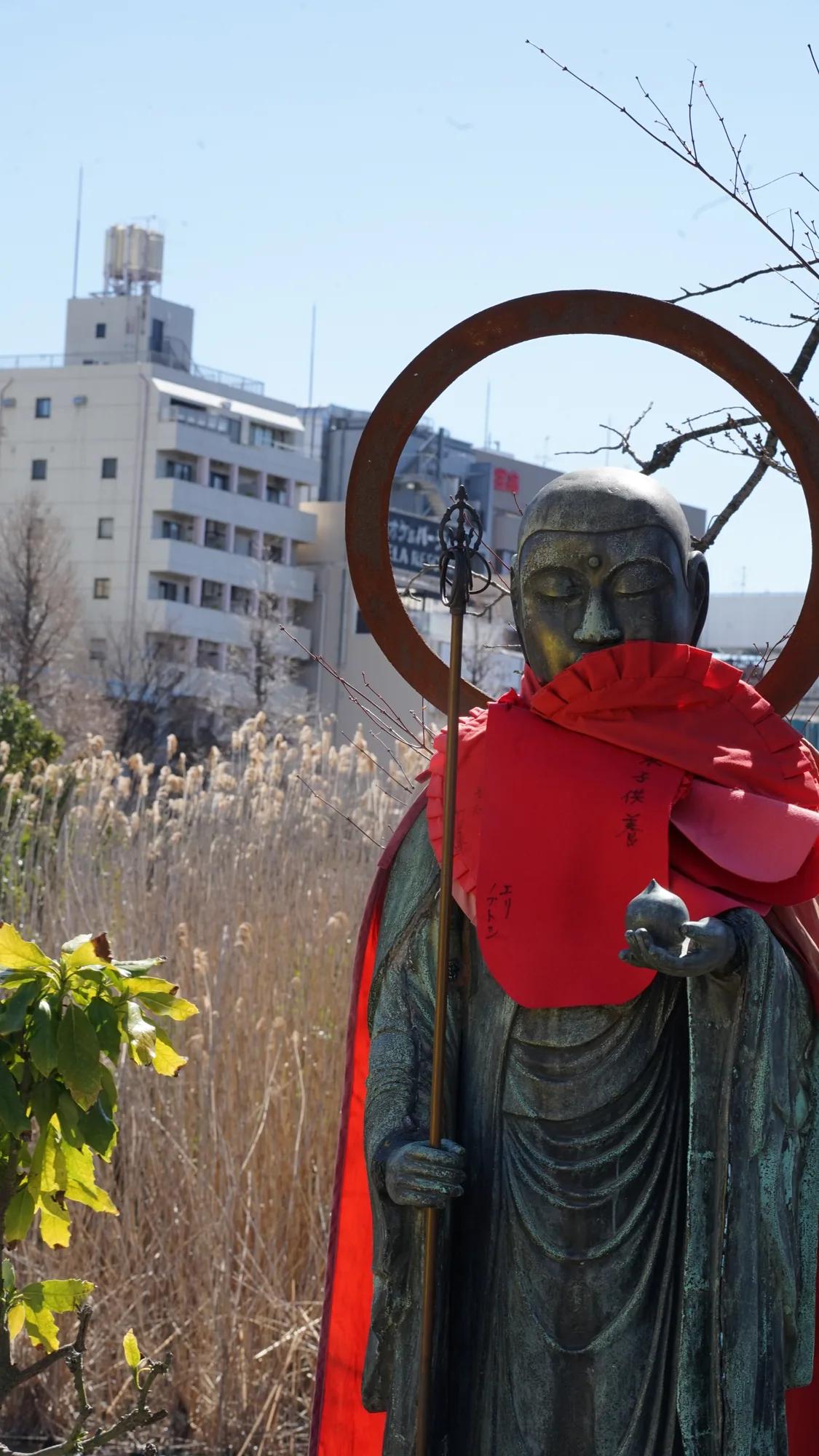 Jizō-Statue mit roten Lätzchen vor Stadtgebäuden in Tokio