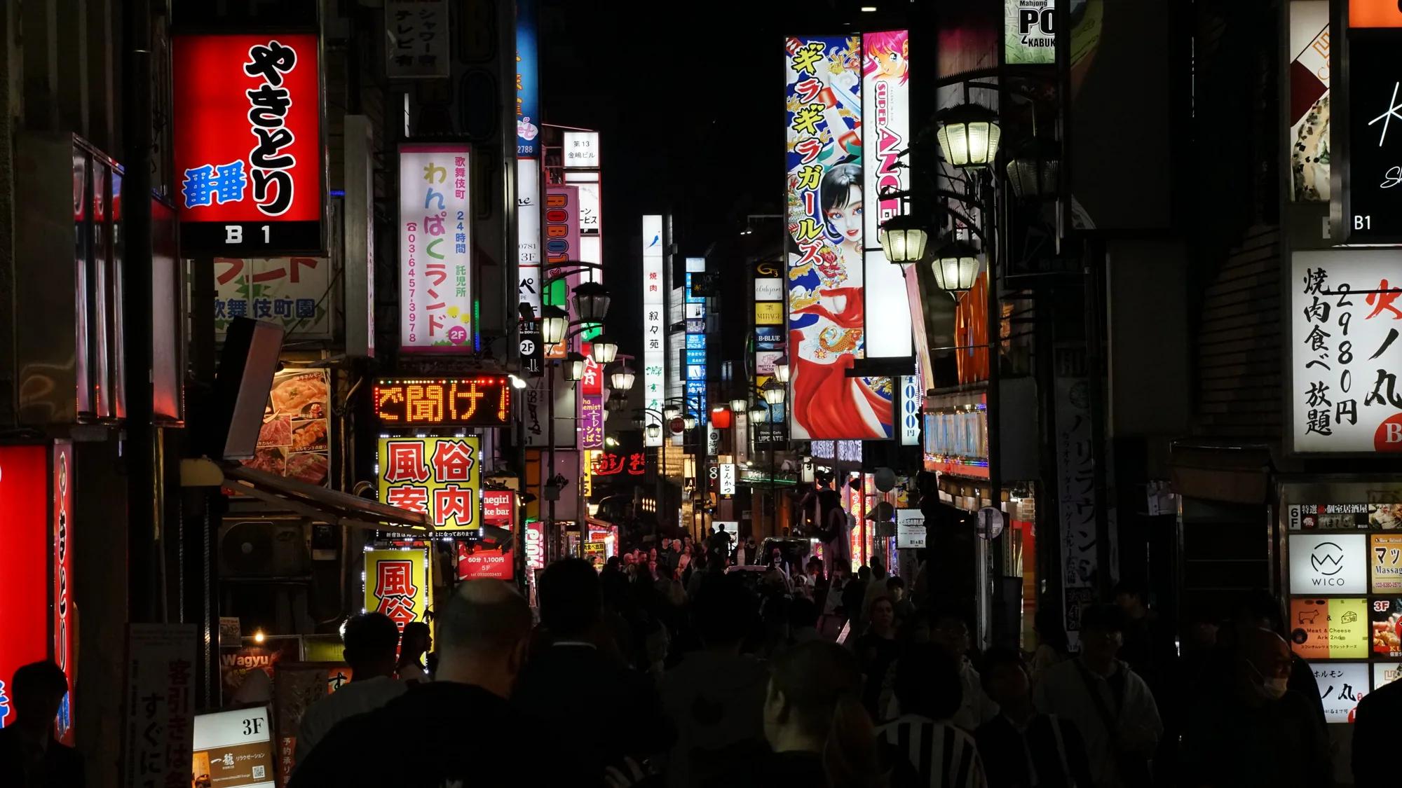 Belebte Straße in Kabukichō mit vielen japanischen Leuchtschildern bei Nacht